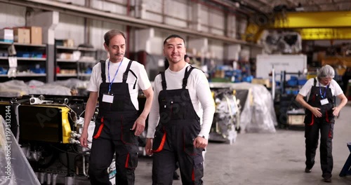 Multi ethnic group of happy mechanics and technicians dancing and celebrating while walking through a large industrial factory warehouse after a successful day of work and production