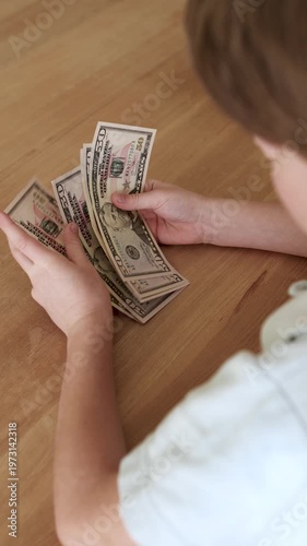 Close up child hands counting new US dollar banknotes. Kid holding cash, learning money value, savings and financial literacy