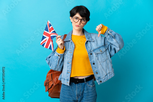 Woman holding an United Kingdom flag over isolated background showing thumb down with negative expression
