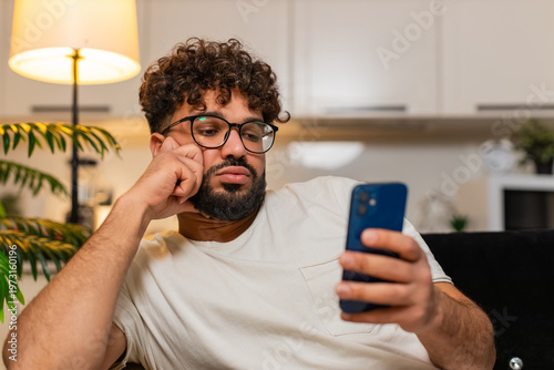 Εκτύπωση καμβά Arabian man at home scrolls smartphone news feels bored tired demotivated sighs shows stress