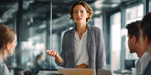 Group of business professionals in modern boardroom meeting, female team leader standing and presenting ideas on whiteboard.