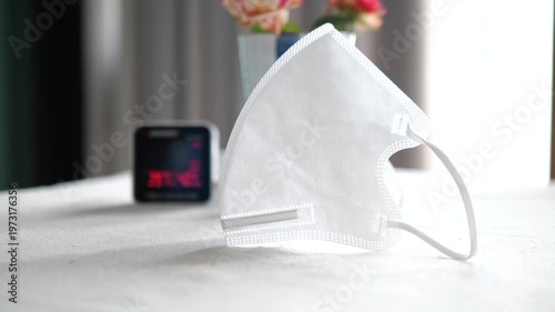 N95 face mask on table with blurred digital air quality monitor showing high PM 2.5 pollution levels for health protection concept