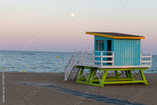 Le Barcarès, cabane de plage sur le sable au coucher du soleil avec la pleine lune au-dessus de la mer Méditerranée, ambiance paisible du littoral dans les Pyrénées-Orientales, Occitanie, France