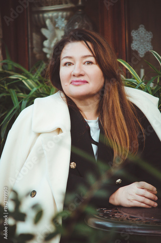 An attractive woman in a white coat sits in a street cafe. Close-up portrait, vertical photo.