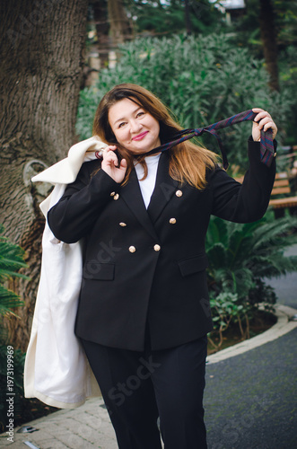 A beautiful middle-aged woman in a business suit smiles happily on the street. Vertical photo.