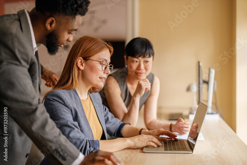 Diverse team of professionals analyzing financial report on laptop while collaborating in business meeting