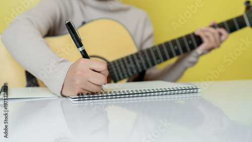 Obraz na płótnie Musician writing music notes in notebook while holding acoustic guitar