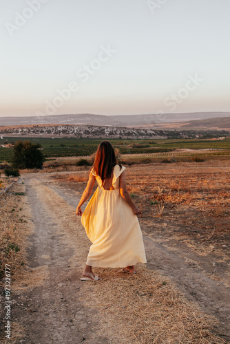 woman in yellow dress walking along path in mountain valley during summer vacation surrounded by scenic landscape and natural beauty concept of travel tourism leisure and outdoor lifestyle