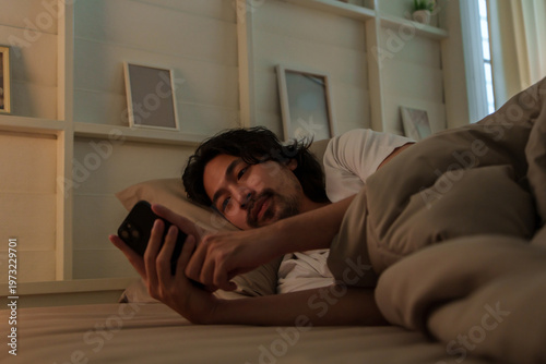 Bilde på lerret Japanese man lying on bed and using smartphone with insomnia at night