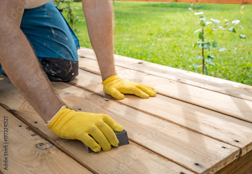 Hands in yellow gloves sand a wooden deck