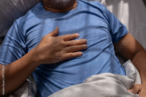 Foto Man holding chest while lying on bed, representing chest pain, heart attack risk, health emergency, cardiovascular problem, medical condition and warning symptoms of serious illness