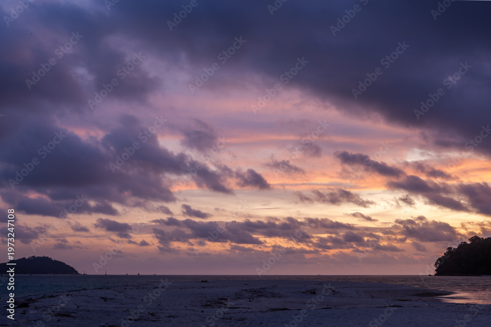 Fototapeta premium Koh Adang sunset. Evening sky fills with purple and orange clouds. Calm Andaman Sea on the horizon. Silhouetted island shore in foreground.