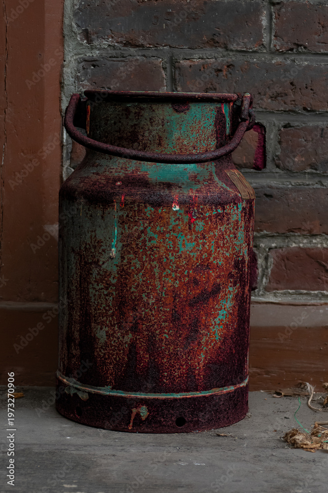 Obraz premium Rusty Vintage Milk Can Against Brick Wall