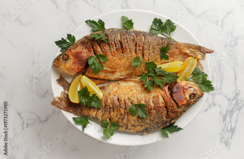 Two baked crucian carp with spices, lemon and parsley. Served on a white plate. Selective Focus, top view