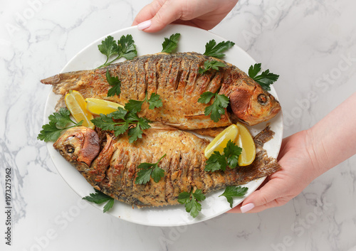 Two baked crucian carp with spices, lemon and parsley. Served on a white plate. Selective Focus, top view