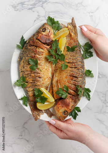 Two baked crucian carp with spices, lemon and parsley. Served on a white plate. Selective Focus, top view