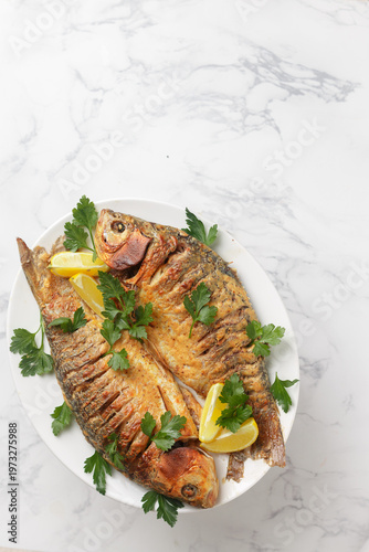 Two baked crucian carp with spices, lemon and parsley. Served on a white plate. Selective Focus, top view, and Copy space