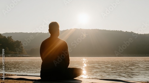Person sits by water at sunrise near mountains
