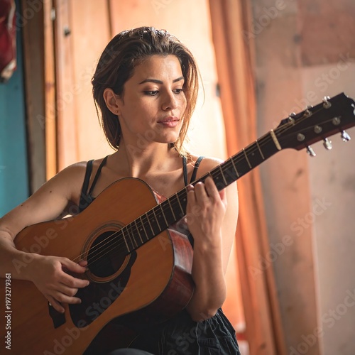 A woman is depicted seated, playing an acoustic guitar. She is focused and looks down at the strings. The lighting is warm