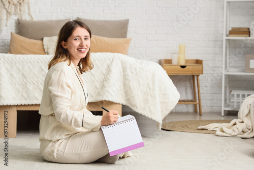 Young woman writing 2026 goals on floor in bedroom