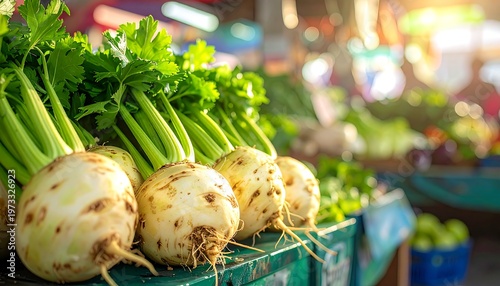 A close-up captures fresh, whole celery roots and stalks on a display table at a market stall under warm sunlight. Other produce is visible in the background