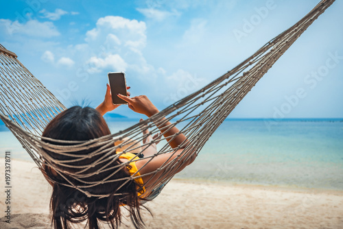 Traveler asian woman relax and use mobile phone and travel in hammock on summer beach at Koh Rap Samui in Surat Thani Thailand