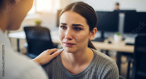 Woman crying at work receiving support from a compassionate colleague, showing empathy and emotional distress in a bright office environment.