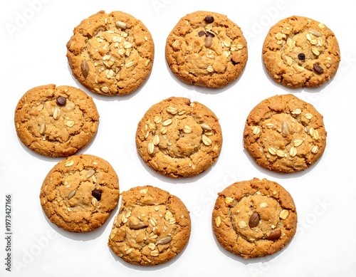 Overhead shot of nine round, golden-brown baked goods with oats, seeds and chocolate chips scattered on a white surface