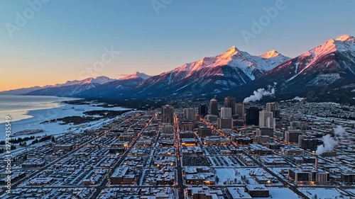 Aerial view of snowy city, frozen lake, and mountains at golden hour