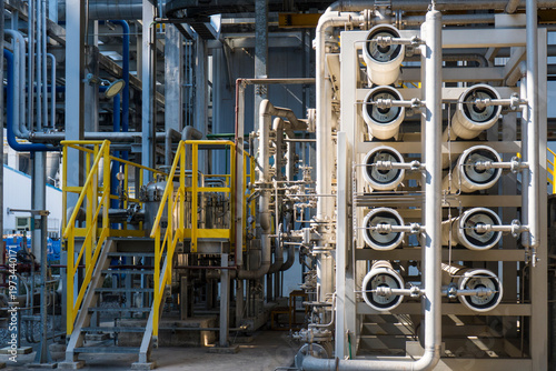 A wide shot of a complex industrial water treatment facility. The image features multiple white reverse osmosis membrane pressure vessels arranged in a rack, connected by a network of stainless steel 