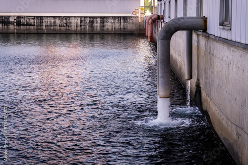 Treated water discharging from large industrial pipes into a collection pool at a factory or treatment facility. The image illustrates industrial water management, drainage systems, and environmental 