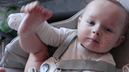 Baby Giggles Explore. Adorable Baby Reaches Out With Joyful Curiosity Indoors. Caucasian Infant In Comfortable Seat Exploring Hands And Feet With Bright Eyes