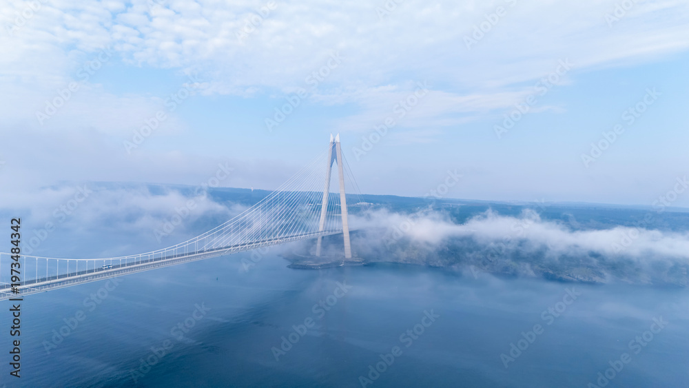 Fototapeta premium Aerial view of Yavuz Sultan Selim Bridge in Istanbul above clouds. Modern bridge pylon through white fog. Ethereal Bosphorus landscape at Poyrazkoy. Atmospheric drone photography.