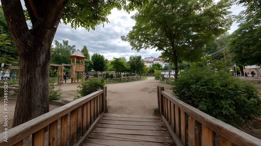 Obraz premium A peaceful wooden walkway leads through a lush park environment towards a distant playground under an overcast sky