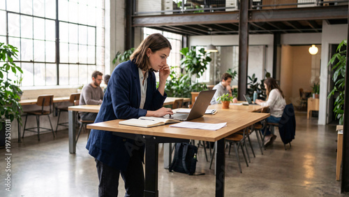 Young Professional Reviewing Documents at Standing Desk in Modern Co-Working Space, Casual Office Attire, Natural Posture, Daylight, Editorial Workspace, Productivity, Work Life