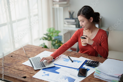 Tableau sur toile Young Asian woman focusing on work, typing on laptop, reviewing financial report