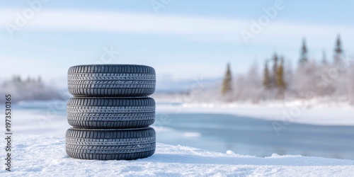 four winter tires stacked on top of each other in the snow, in front of a frozen lake with a clear sky.