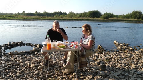 A man and woman had a picnic on the riverbank, enjoying food and drinks.