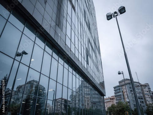 Modern Glass Office Building Facade Reflecting Cityscape Under Cloudy Sky.
