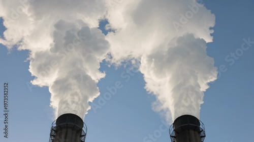 Industrial chimneys emitting thick white smoke against a clear blue sky.