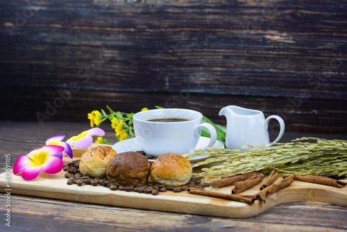 Still life coffee scene with cup of black coffee, bread, coffee beans, sunflower and cinnamon on wooden background, warm cozy cafe