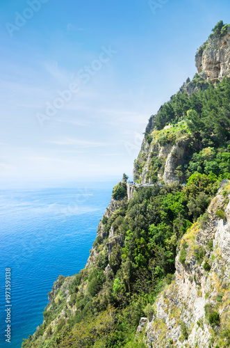 Coastal road along the cliffs of Amalfi Coast, Italy, with views of Mediterranean Sea. Rugged mountains and lush greenery in sunny day