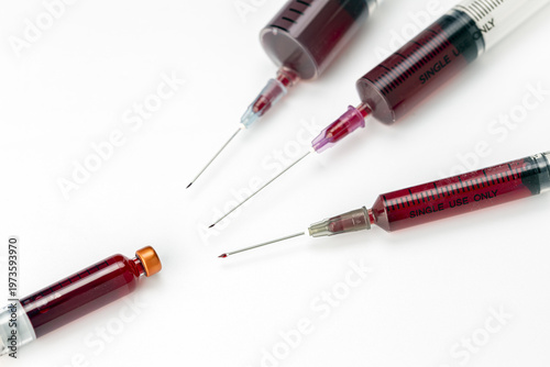 Close-Up of Multiple Medical Syringes Filled With Dark Red Blood Samples and Sharp Needles Arranged on a Clean White Background for Healthcare Concepts
