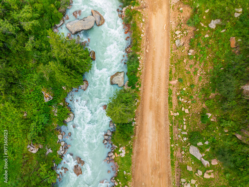 Fotografija Serene mountain river flows alongside unpaved dirt road in Kyrgyzstan