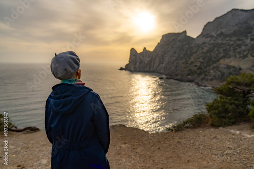 Woman sunset sea watching dramatic golden ocean view from rocky cliff edge