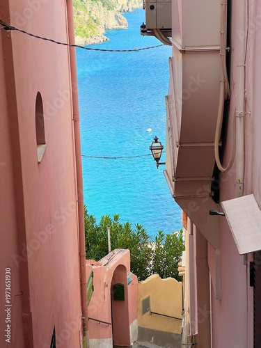 Narrow alley in Positano with pastel walls and view of turquoise sea, capturing intimate Mediterranean charm, coastal architecture, and peaceful Italian village atmosphere.