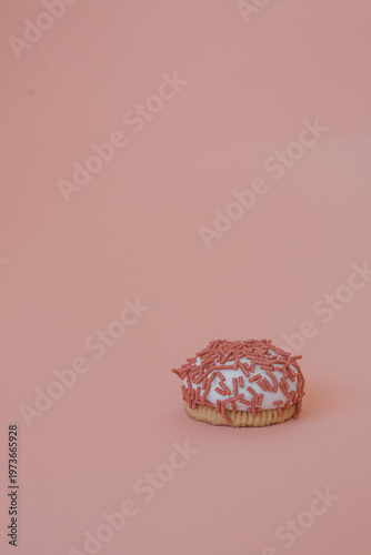Dessert petit four with pink sprinkles on a pink background. Festive treat. Shortbread. Dessert with copy space. Sweet food for coffee. Exquisite mini cake. Fast carbohydrates. Diet violation.