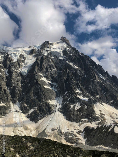 Aiguille du Midi, Mont blanc massif showing rugged rock faces and expansive glaciers under a dynamic sky with white clouds, highlighting the grandeur of the alps - stock photo
