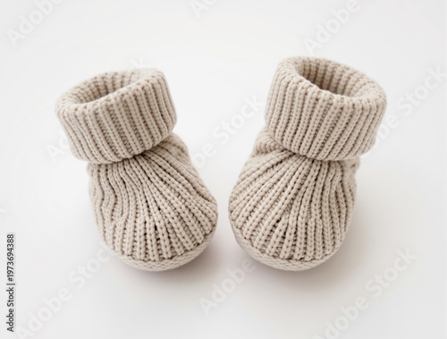 Cozy knitted baby booties in soft neutral beige, featuring ribbed cuffs and a textured knit, presented against a clean white background, evoking warmth and comfort.
