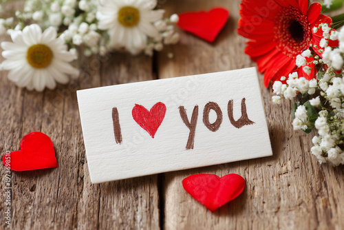 Words of love on a card with flowers and hearts on a wooden table